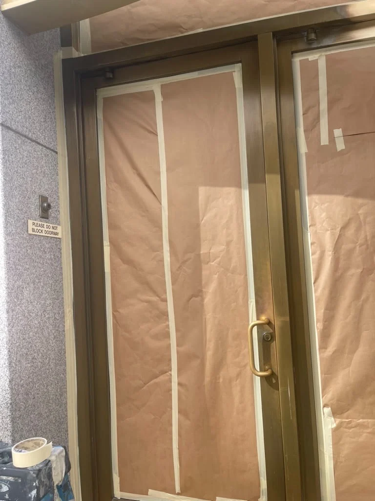 Brass entrance door and frame with the glass masked off during refinishing in Newark, New Jersey