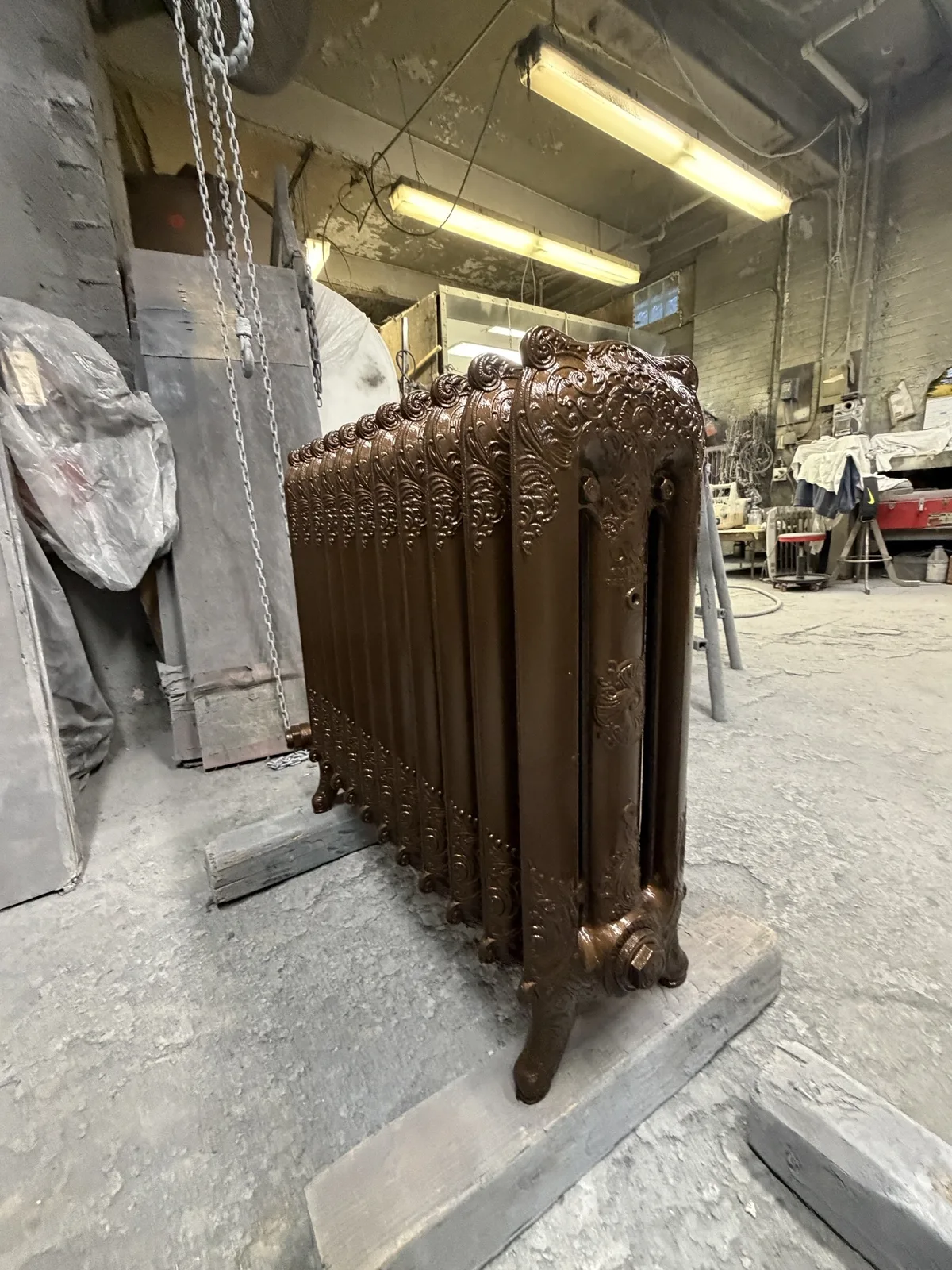 Restored cast iron radiator in a bronze metallic finish, standing in the Metal Man Restoration shop