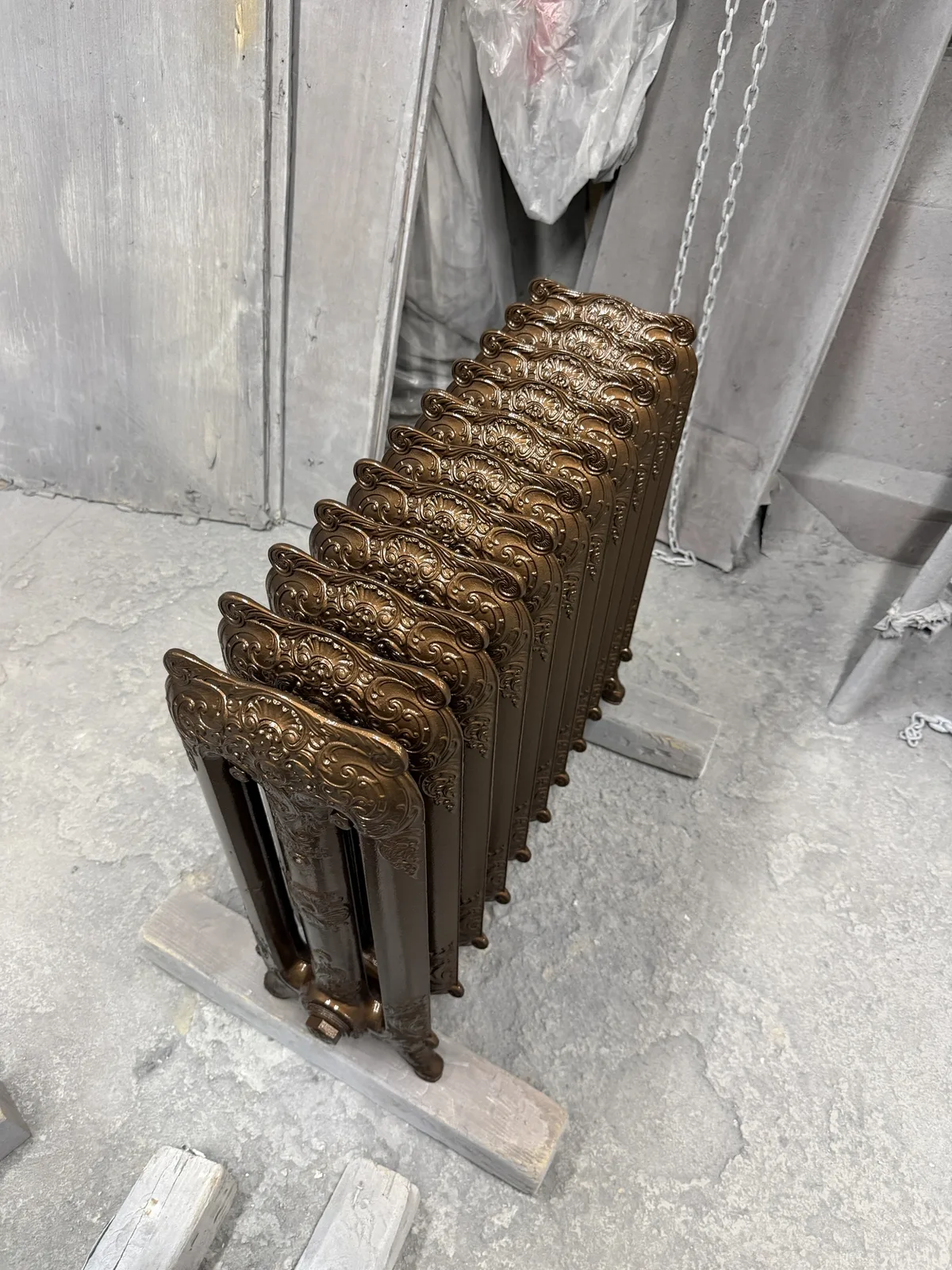 Side view of the restored cast iron radiator showing the ornate cast detail in a metallic finish